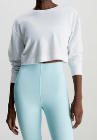 White cropped sweatshirt with Calvin Klein logo, paired with high-waisted, light blue glossy leggings, showcasing smooth texture and fitted design.