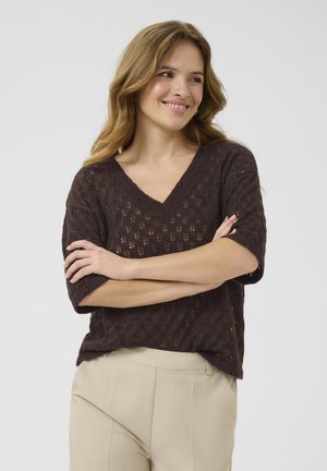 Brown, V-neck knit sweater with short sleeves featuring a textured, open weave pattern. Paired with light beige trousers.