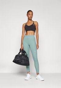 Czarny stanik sportowy, legginsy w kolorze miętowym z logo, czarna torba sportowa z siateczkową sekcją oraz białe buty sportowe. Prosty i funkcjonalny design.