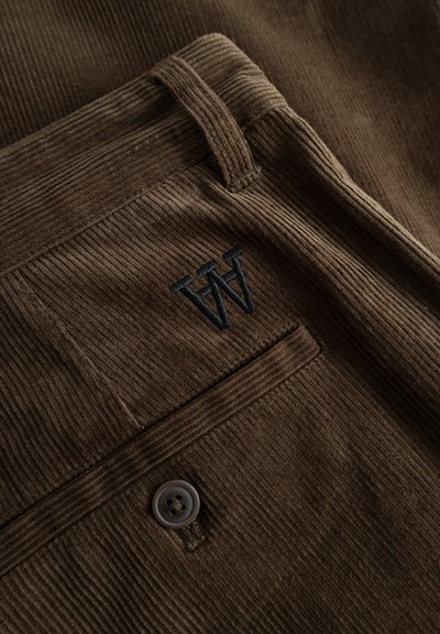 Tissu en velours côtelé marron avec des côtes verticales, comprenant un bouton, une poche et un logo "W" brodé en noir. Design texturé et durable.