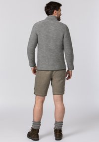 Grauer gestrickter Pullover mit hohem Kragen, kombiniert mit hellbraunen Shorts. Das Modell trägt graue umgeschlagene Socken und braune Stiefel.