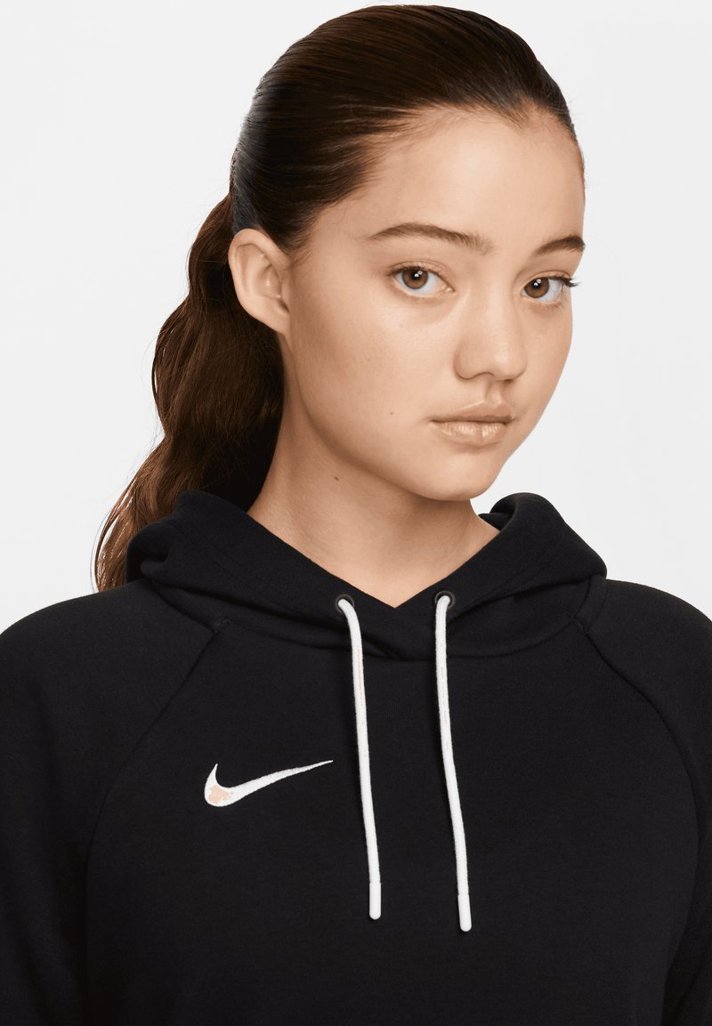 Felpa nera Nike presenta un logo bianco sul petto, con cordini e un tessuto strutturato. Il viso del modello mostra un'espressione neutra, sfondo chiaro.