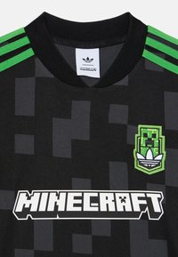 Čierny športový dres so zelenými pruhmi na ramenách, pixelová textúra, logo Minecraft a vyšívaná nášivka Adidas na hrudi.
