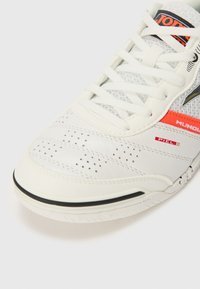 Sneaker in pelle bianca con dettagli perforati, punta tonda, inserti in rete e lacci bianchi. Presenta un logo nero e arancione lungo il lato.