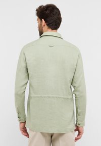 Lichtgroene blouse met lange mouwen, een button-down kraag, een rugpasdetail en knoopmanchetten. Gemaakt van textuur linnen stof.