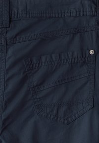 Granatowy materiał spodni z tylną kieszenią z ukośnym przeszyciem i srebrnym guzikiem. Gładka i lekko błyszcząca tekstura.