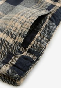 Grosgrain audinys su tamsiai mėlynais, smėlio ir pilkais atspalviais. Medvilnės mišinys, tekstūruotas paviršius, turi sulankstytą apykaklės kraštą ir matomas siuvimo akcentus.