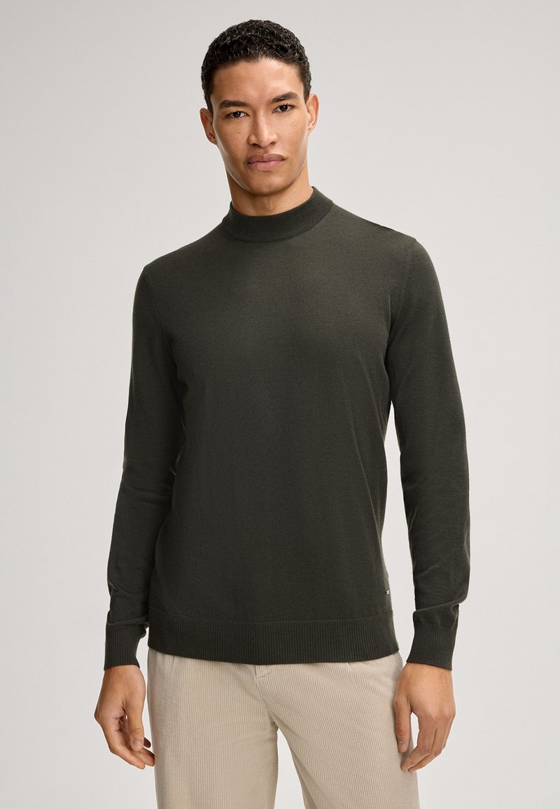Dunkelgrüner, langärmeliger Rollkragenpullover aus glattem Strickmaterial, mit gerippten Bündchen und Saum. Über hellen Hosen getragen.