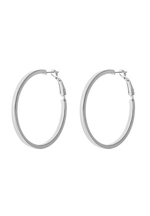 Paire de boucles d'oreilles créoles lisses en argent avec des bandes fines et arrondies et des fermoirs à charnières sur fond blanc.