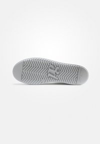 Semelle de chaussure en caoutchouc blanc avec un motif de chevrons texturée, présentant un logo en relief et un capuchon de orteil lisse.
