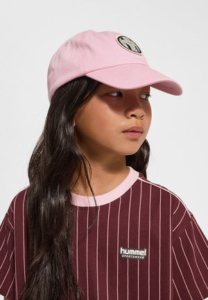 Rosa basebollkeps med ett runt svart emblem på framsidan, bärs med en vinröd randig t-shirt med en logotyp på bröstet.