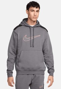 Felpa grigia con tasca a marsupio, dettagli neri sulle spalle e logo Nike rosa sul petto. Realizzata in tessuto morbido e strutturato.