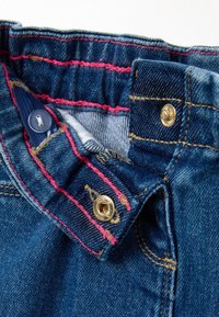 Cintura de jeans de mezclilla con costuras rosas en contraste, botón de hardware dorado y cierre de botón azul. Textura suave y lavado oscuro.