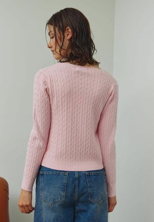 Ružový sveter s pleteným vzorom, s rebrovanými manžetami a lemom, vybavený klasickým okrúhlym výstrihom a textúrovaným vzorom. Nosený s džínsami s vysokým pásom.