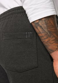 Donkergrijze sweatpants met een elastische tailleband, voorzien van een achterzak en een subtiele "JP"-logo. De stof lijkt zacht en gestructureerd.