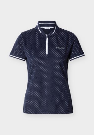 Marineblå kortermet polo med hvite polkadotter, hvite striper på krage og mansjetter, halvglidelås foran og "Calvin Klein"-logo på brystet.