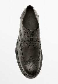 Chaussure habillée en cuir noir avec un design à bout pointu perforé, cinq œillets, bout arrondi et coutures décoratives le long de la semelle.