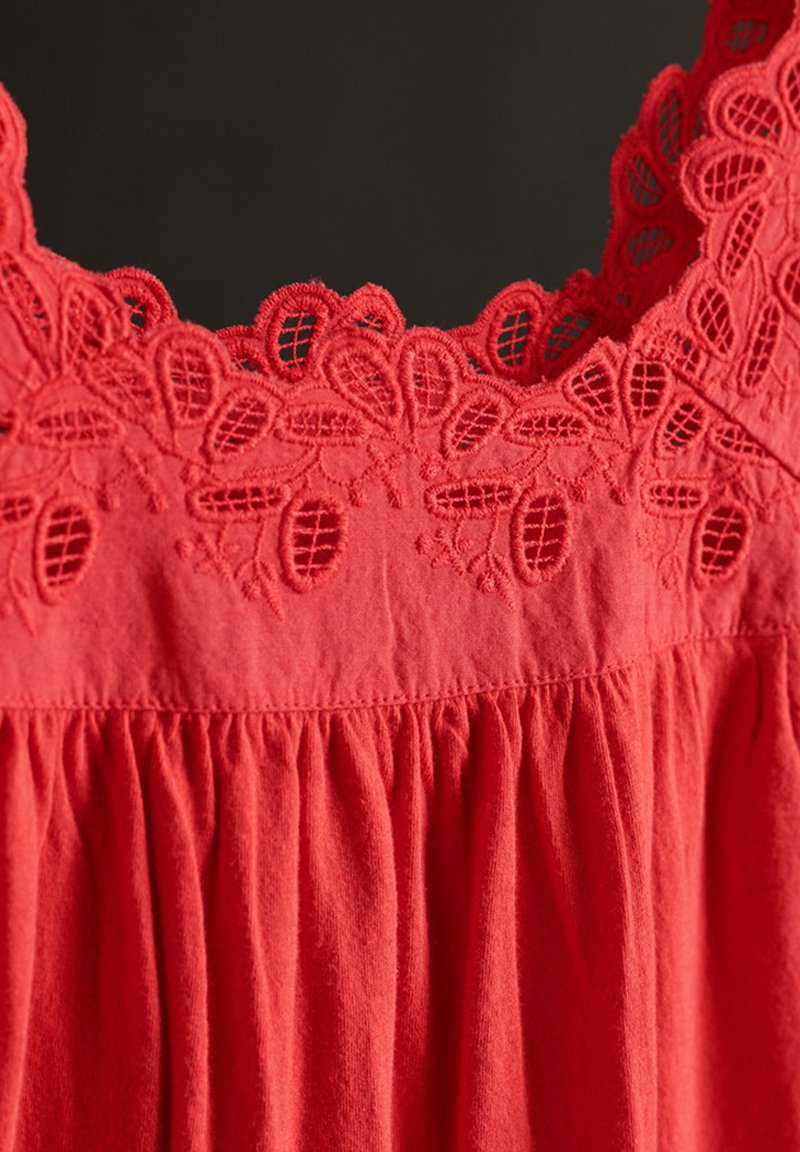 Abito senza maniche rosso con scollatura in pizzo a onde, dettagli arricciati nella parte inferiore e un tessuto morbido e strutturato.