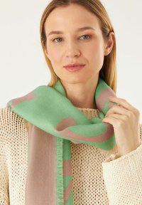 Groene en roze gestreepte sjaal gemaakt van zachte stof, met franjes en een gladde textuur, om de schouders gedrapeerd.