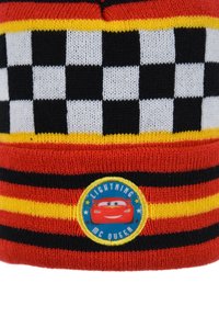 Red, black, and yellow knit beanie featuring a checkered pattern, with a circular Lightning McQueen patch on the front. Soft texture.