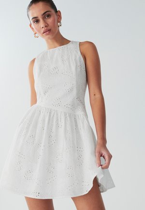 Witte mouwloze jurk van gestructureerde stof met gaatjesdetails. Uitlopende rok met een ronde zoom, die subtiele bloempatronen laat zien.