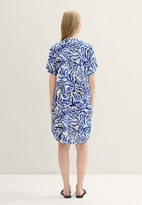 Modrá a bílá vzorovaná šaty s volným střihem, krátkými rukávy, kulatým výstřihem a zakřiveným lemem. Texturovaná tkanina s abstraktními pruhy.