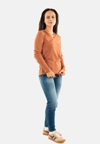 Maglietta a maniche lunghe color arancio bruciato con scollatura a V; texture morbida. Abbinata a jeans skinny blu medio e sneakers casual multicolori.