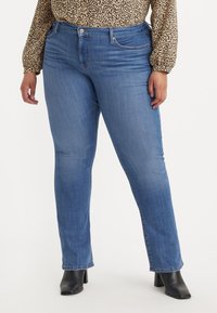 Jeans in denim blu chiaro con una vestibilità a gamba dritta. Presentano un giro vita a media altezza, un classico design a cinque tasche e una leggera scoloritura. Stivali neri con tacco mostrati.