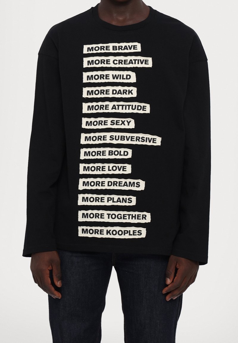 Felpa nera a maniche lunghe con testo sovrapposto color crema in grassetto e in stile ritagliato che esprime diverse affermazioni allineate verticalmente.