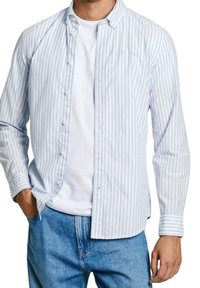 Camicia button-up a righe blu chiaro e bianche con una texture morbida, maniche lunghe e colletto classico, indossata sopra una maglietta bianca.