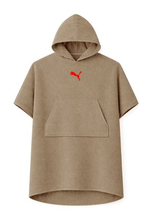 Mann trägt einen khakifarbenen Kapuzen-Handtuchponcho mit rotem Puma-Logo, Hände in der Vordertasche, steht vor einem einfarbigen Hintergrund.