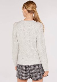Ljusgrå stickad tröja med ribbad textur och ett zick-zack mönster, rund halsringning och långa ärmar, tillsammans med mönstrade shorts.