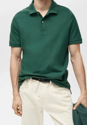 Grøn polo med korte ærmer, to knapper ved kraven og en glat tekstur, kombineret med lysebeige bukser.