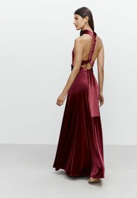 Bordeaux-rotes Satin-Maxikleid mit Halterneck, offenem Rücken und verdrehtem Stoffdetail am Ausschnitt. Glatte Textur und fließendes Design.