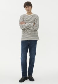 Csíkos, bézs és sötétkék hosszú ujjú ing, párosítva sötétkék farmernadrággal és fekete cipővel. Egyszerű, laza fazon.