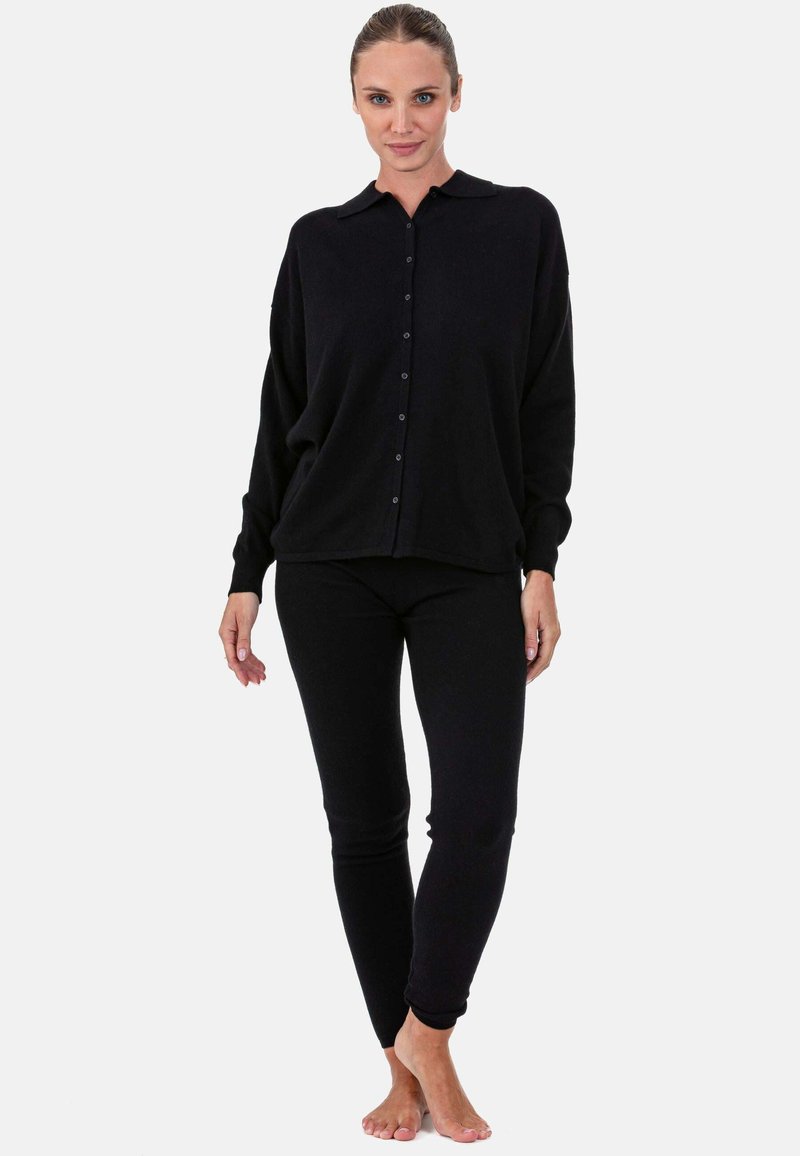 Chemise noire en maille boutonnée avec col, associée à un pantalon ajusté assorti. Texture douce, coupe ample et manches longues. Le mannequin est pieds nus.