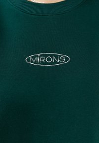 Sweatshirt verde con un collo a girocotone a costine, caratterizzato da un logo a forma ovale "MIRONS" adornato di strass sul petto. Tessuto morbido.