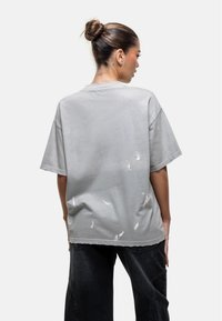 Szary, oversize t-shirt z postrzępionymi detalami i postrzępionymi końcówkami. Wykonany z bawełny, z okrągłym dekoltem i luźnym krojem.