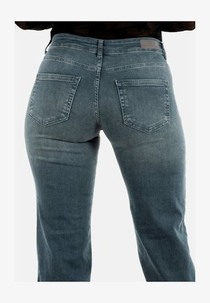 Achteraanzicht van een persoon in een blauwe spijkerbroek met twee achterzakken en een leren label op de tailleband.