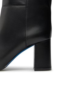 Primo piano di un stivale alla caviglia in pelle nera con tacco a blocco e cuciture visibili lungo il pannello laterale.