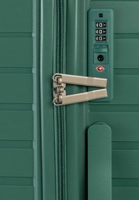 Maleta rígida verde con textura estriada, cerradura combinada y cierre de doble cremallera. Cuenta con un candado TSA. Materiales duraderos utilizados.