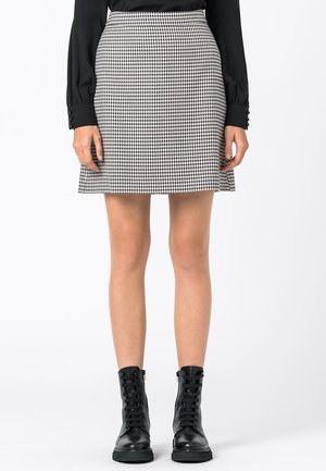 Jupe pied-de-poule noir et blanc avec une silhouette évasée, dotée d'une taille haute et d'une texture lisse, associée à des bottes noires à lacets.