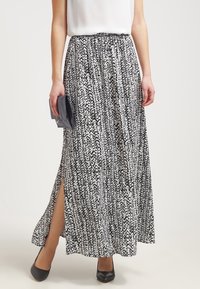 Maxikjol i svart och vitt mönster, tillverkad av lättviktsmaterial. Har en smockad midja och splittar på sidorna. Kombinerad med en clutch och klackar.