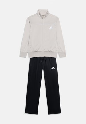 Chaqueta deportiva gris claro con cremallera y logo blanco, combinada con pantalones deportivos negros con logo blanco a juego.