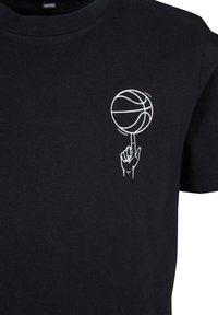 T-shirt en coton noir avec un graphique blanc représentant une main équilibrant un basketball sur le bout de son doigt. Manches courtes et col rond.