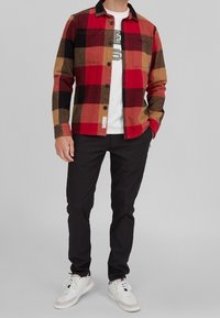 Punainen ja musta ruudullinen flanelliapaita mustalla kauluksella ja napituksella, valkoisen graafisen t-paidan päällä. Yhdistetty mustiin housuihin ja valkoisiin lenkkareihin.