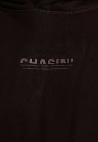 Felpa con cappuccio nera caratterizzata da un marchio stampato "CHASIN'" e un logo testuale di colore più chiaro. Tessuto testurizzato con una finitura liscia.