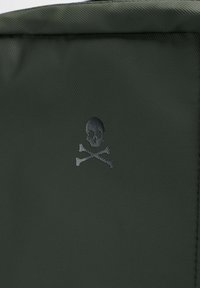 Tejido texturizado de color verde oscuro con un logo de calavera y tibias en negro. El diseño es minimalista, sin adornos adicionales.