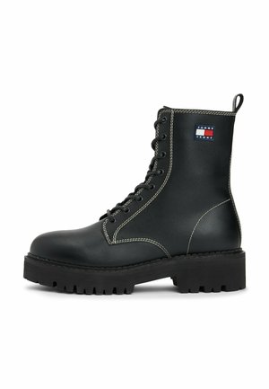 Botte en cuir noir à lacets avec semelle épaisse, coutures blanches, tirette et patch logo Tommy Jeans sur le côté.