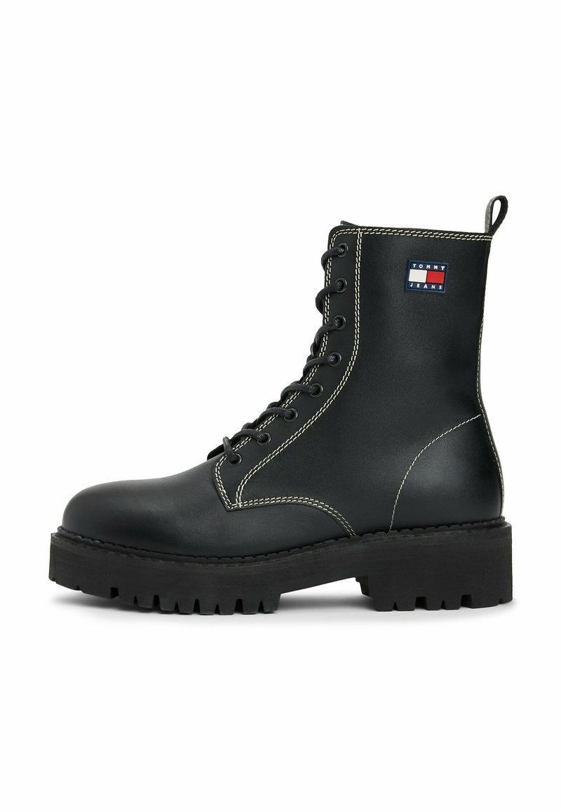 Botín de cuero negro con cordones, suela gruesa, costuras blancas, tirador y parche del logo de Tommy Jeans en el costado.